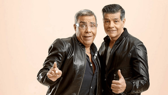A la izquierda vemos  Juan Salazar luciendo un look de chaqueta de cuero con una camisa debajo. Sonriente, con el brazo estirado y el dedo índice hacia arriba, luce unas gafas transparentes muy modernas. Además, lleva unas gafas transparentes y modernas. A la derecha de la imagen está su hermano José con un look combinado por la chaqueta de cuero y una camiseta gris que se entre deja ver debajo. También aparece sonriente con el dedo pulgar hacia arriba.  